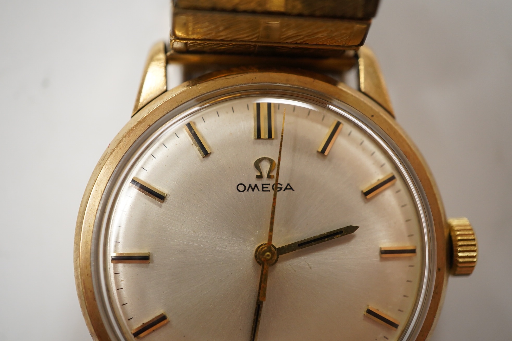 A gentleman's yellow metal Omega manual wind wrist watch, with baton numerals, case diameter 34mm, on an associated rolled gold flexible strap. Condition - fair